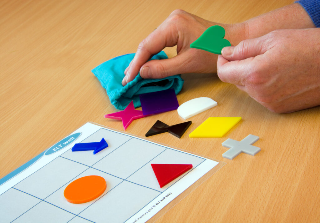 A person arranges coloured shapes on a grid.